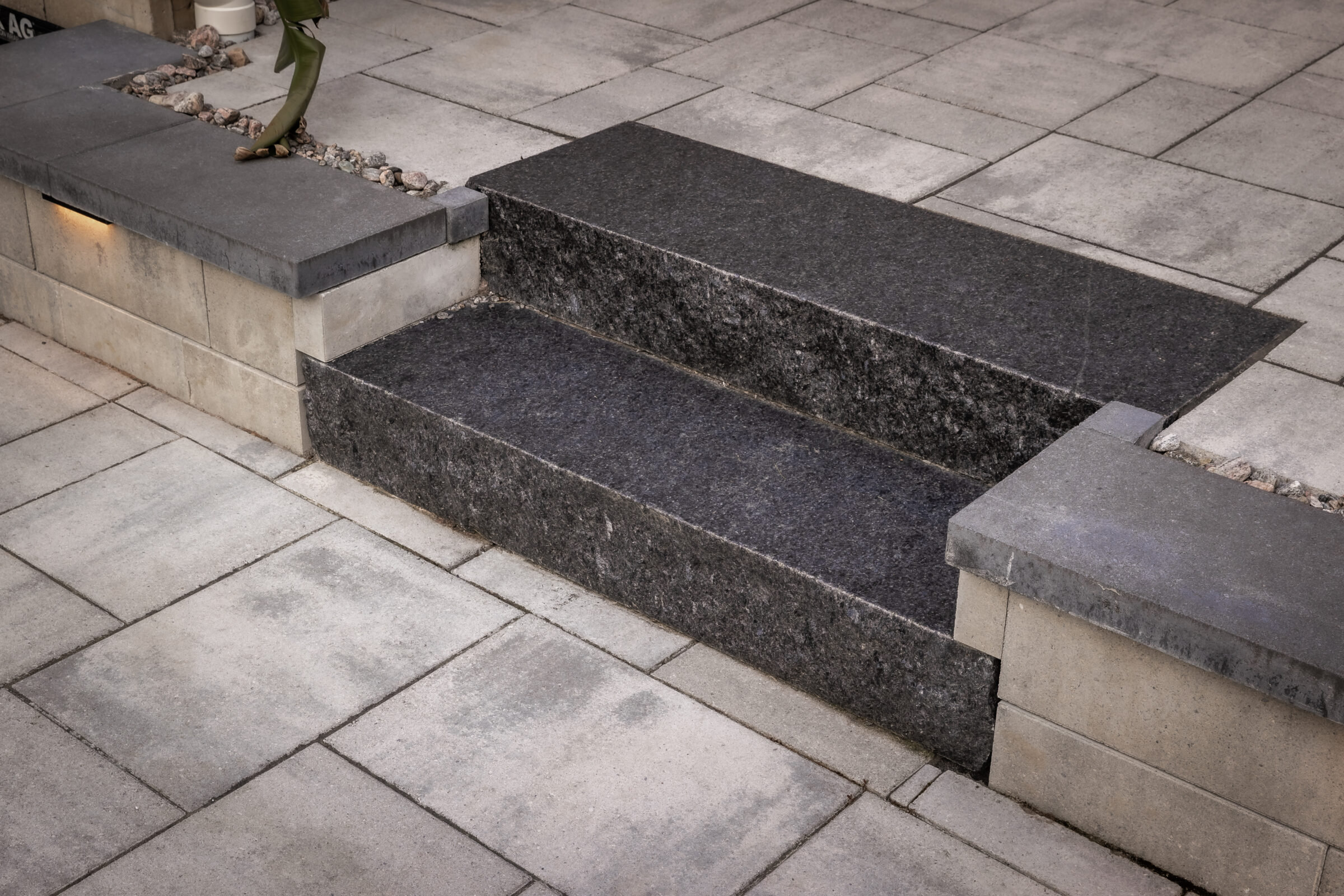Gray stone steps and surrounding concrete tiles in a modern outdoor patio setting, with a small plant visible at the corner.