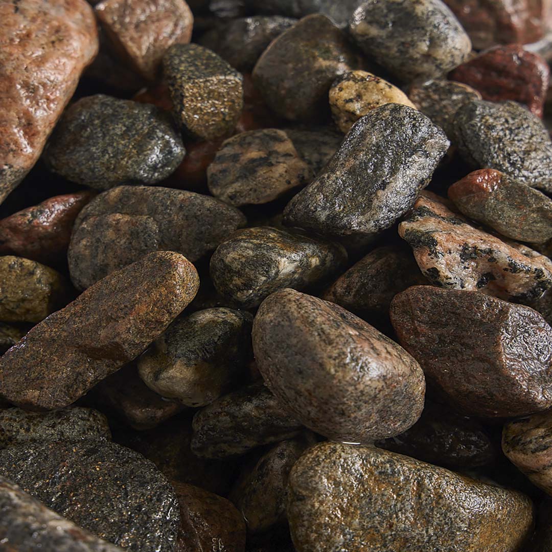 A close-up image of various smooth, multicolored rocks and pebbles. The stones display natural texture and earthy tones, creating a rustic appearance.