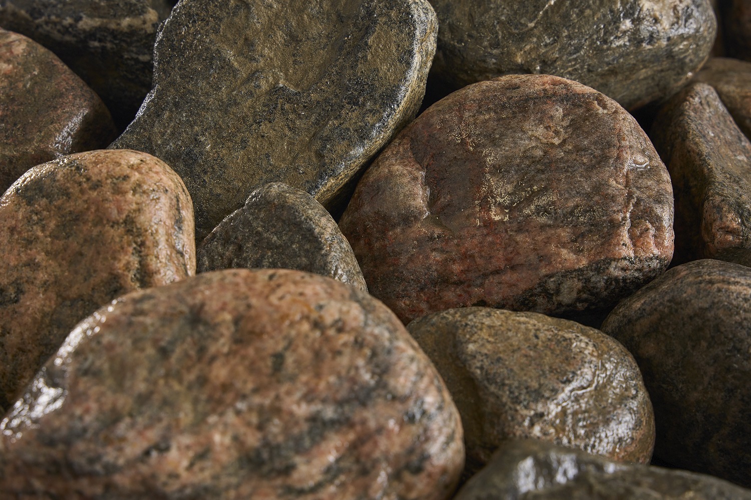 A close-up image of several smooth, multi-colored rocks, showcasing their textured surfaces with shades of grey, brown, and hints of red.