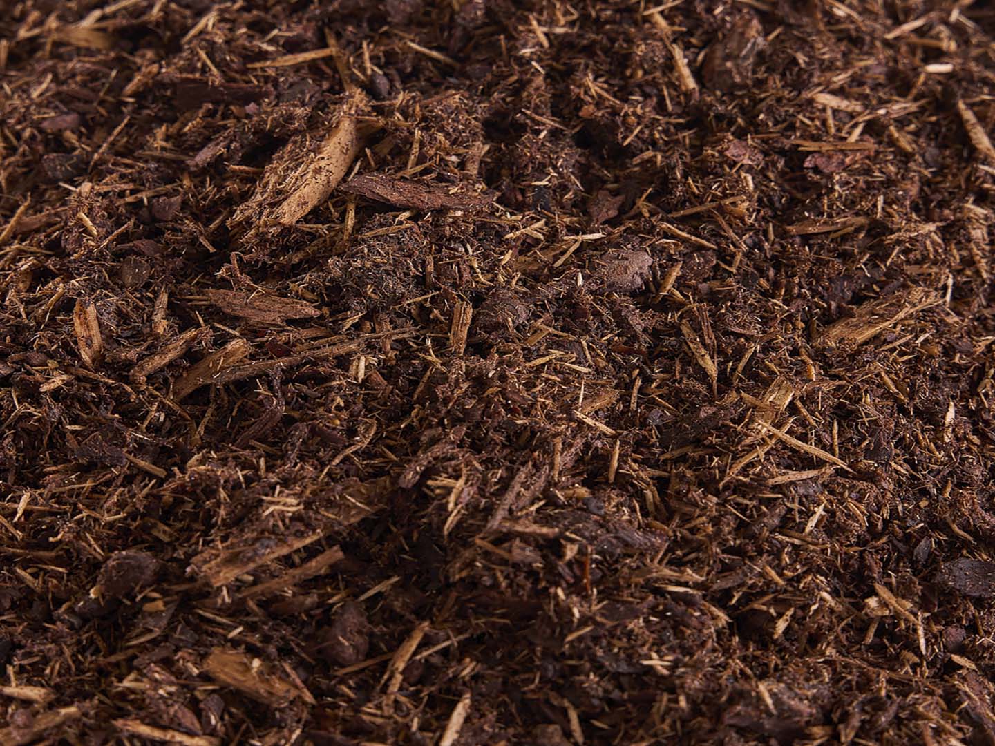 A close-up of brown mulch featuring small wood chips and organic material, providing a textured view of the gardening material.