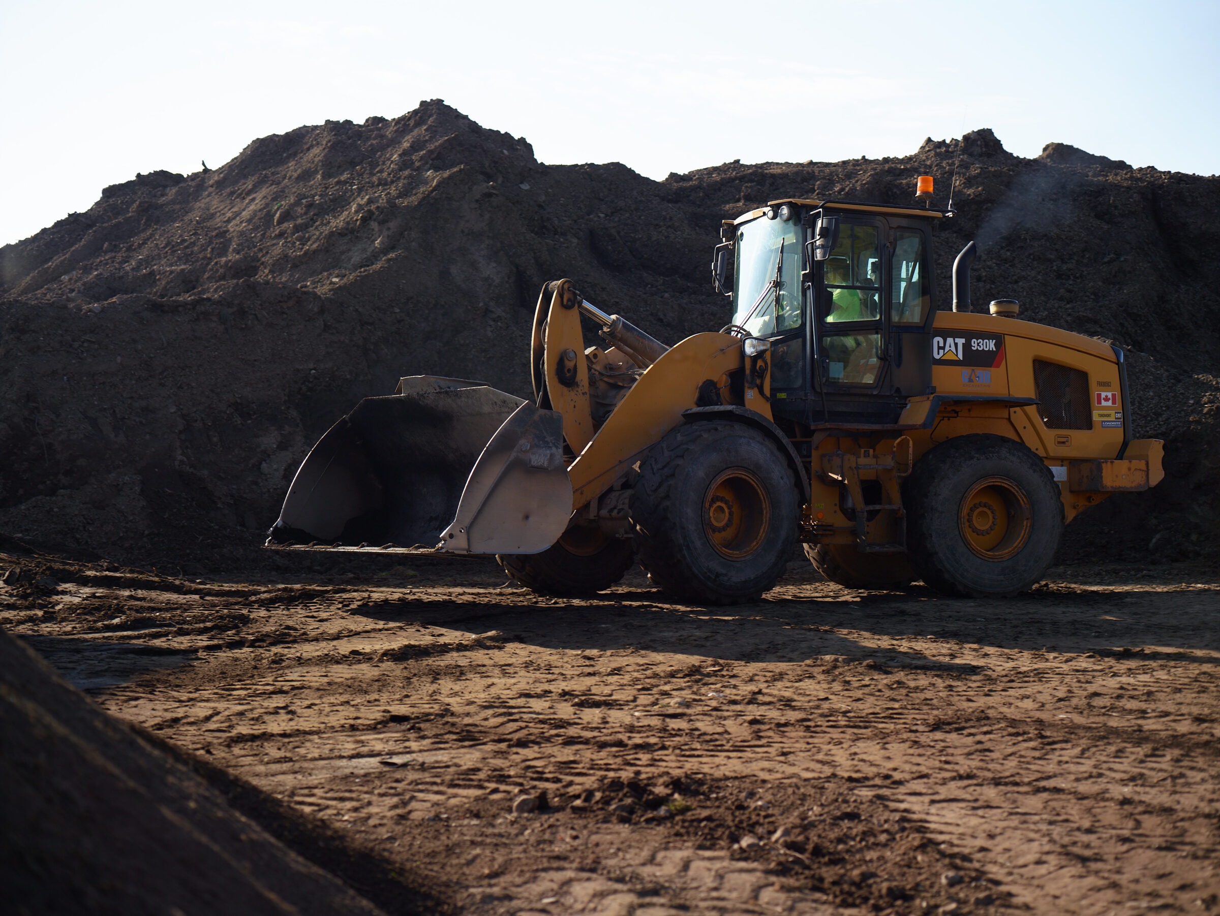 A yellow Caterpillar front-loader stands idle at a construction site, surrounded by large mounds of dirt under a clear sky.