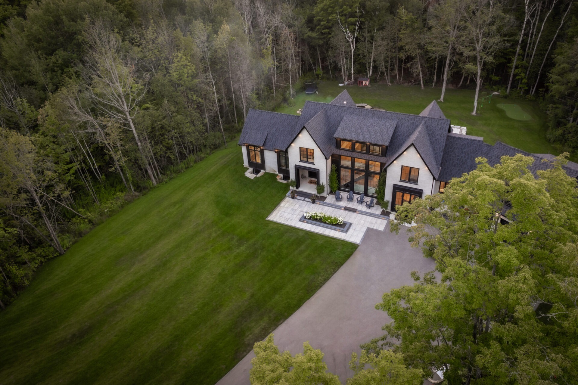 Aerial view of a large, modern house surrounded by lush trees and an expansive lawn, nestled in a serene, wooded area.