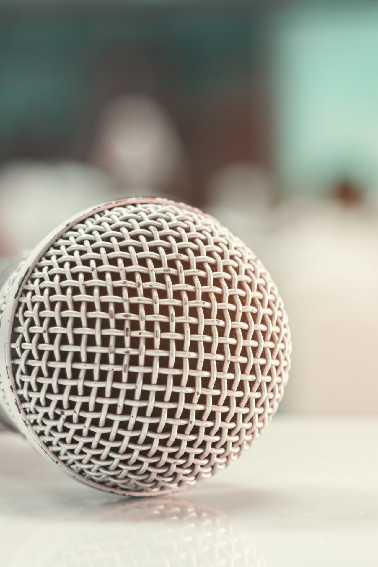 A silver microphone with a mesh grille is in sharp focus, positioned against a blurred background, hinting at a recording or performance setting.